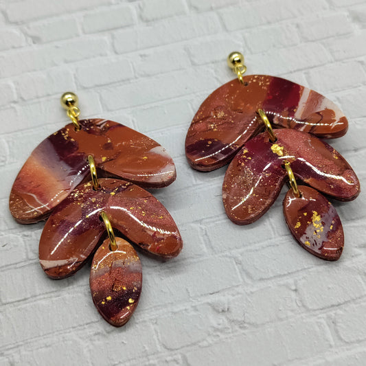 Pair of brown and gold leaf-shaped earrings on a textured gray background