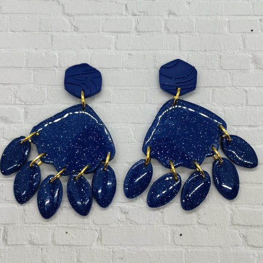 Pair of blue glittery earrings with gold accents on a white brick wall background