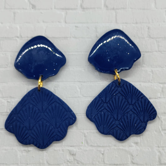 Pair of blue earrings with textured design on a white brick background