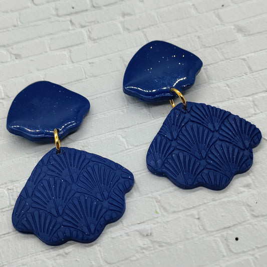 Pair of blue textured earrings on a white brick background