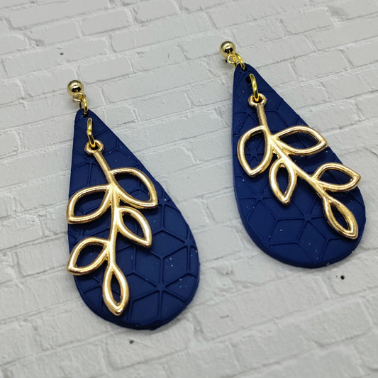 Navy blue earrings with gold leaf designs on a textured gray background