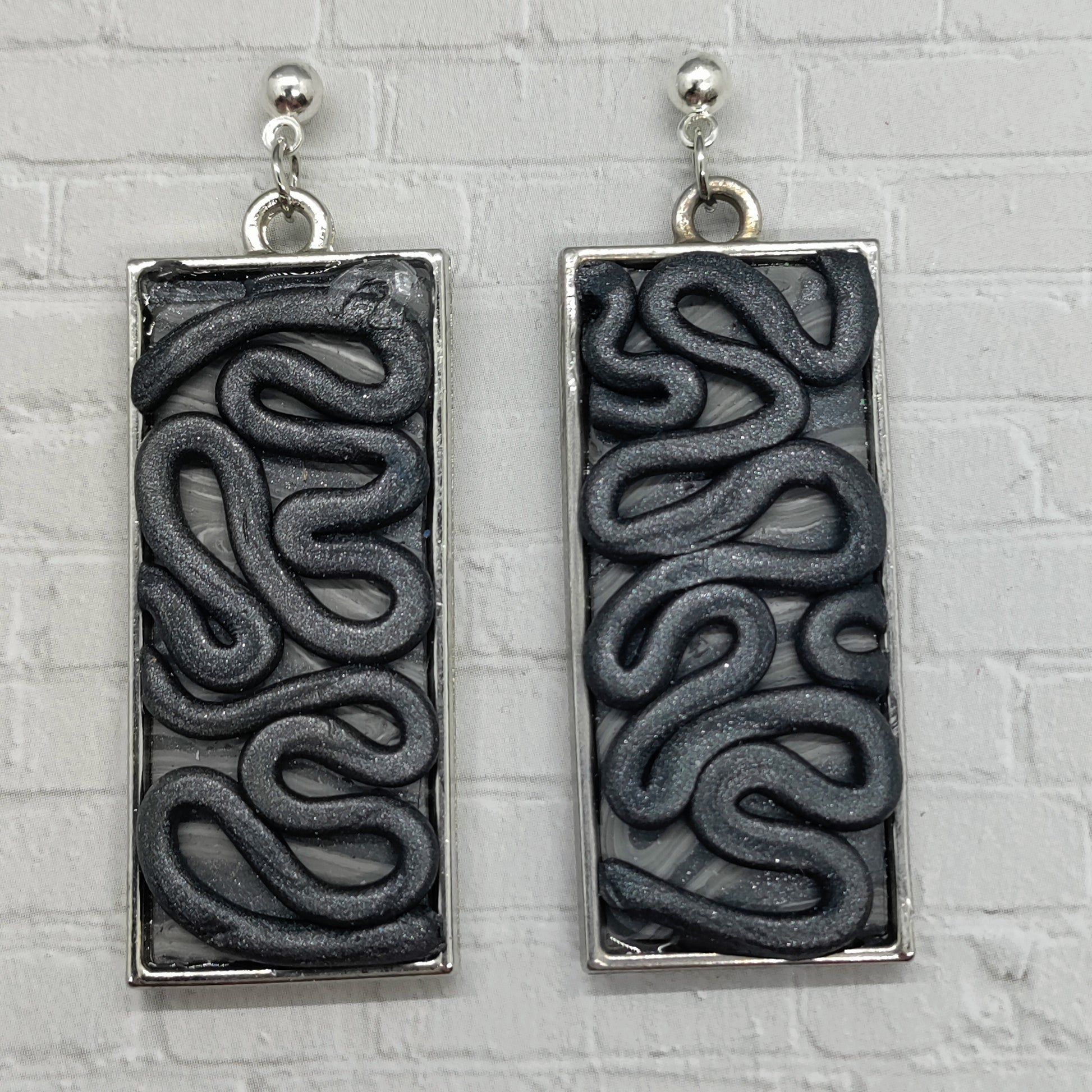 Pair of rectangular earrings with wavy pattern on a textured gray background