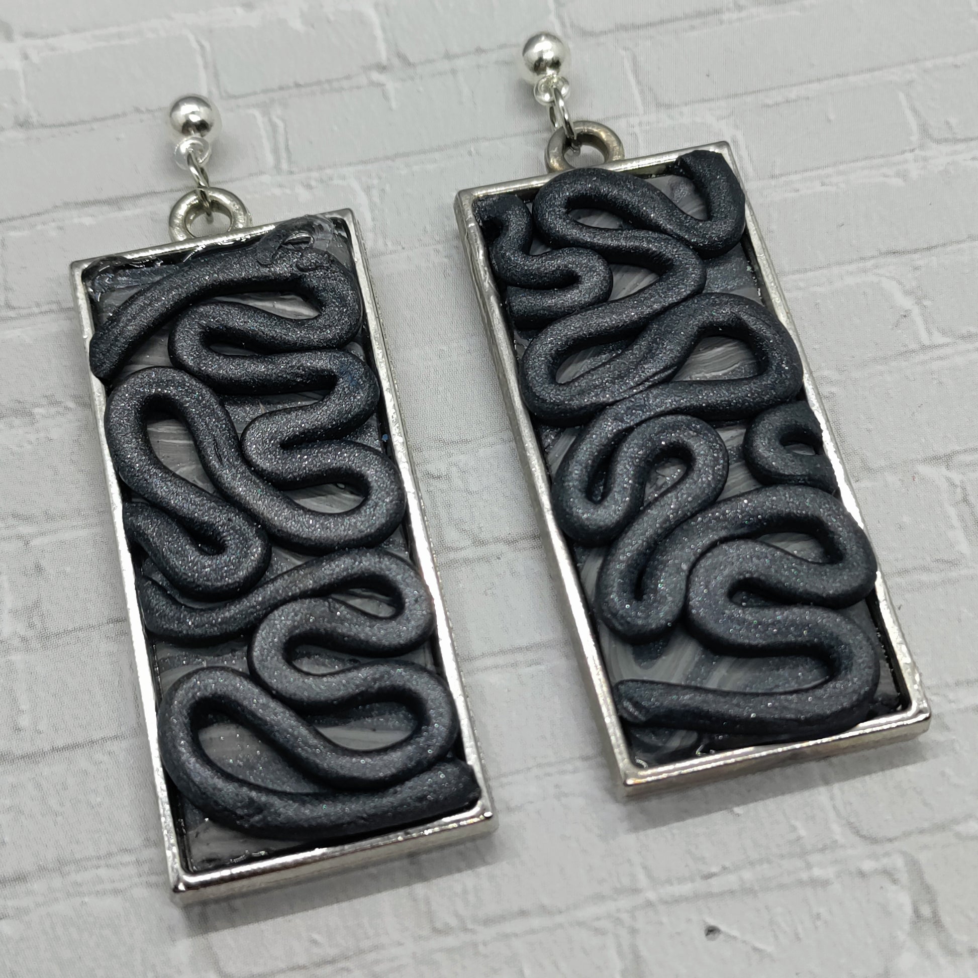 Black wavy patterned earrings on a gray background