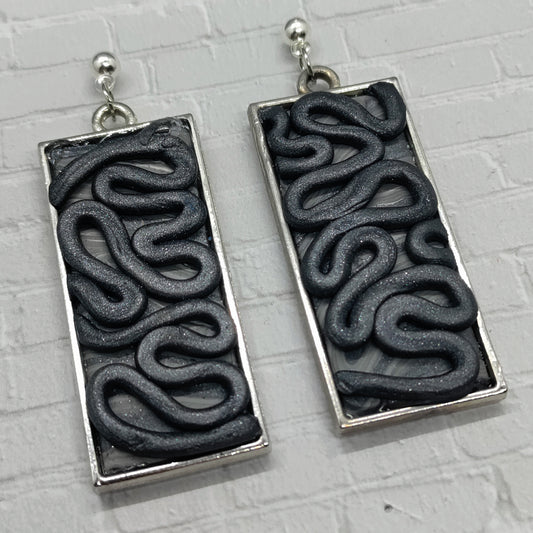 Black wavy patterned earrings on a gray background