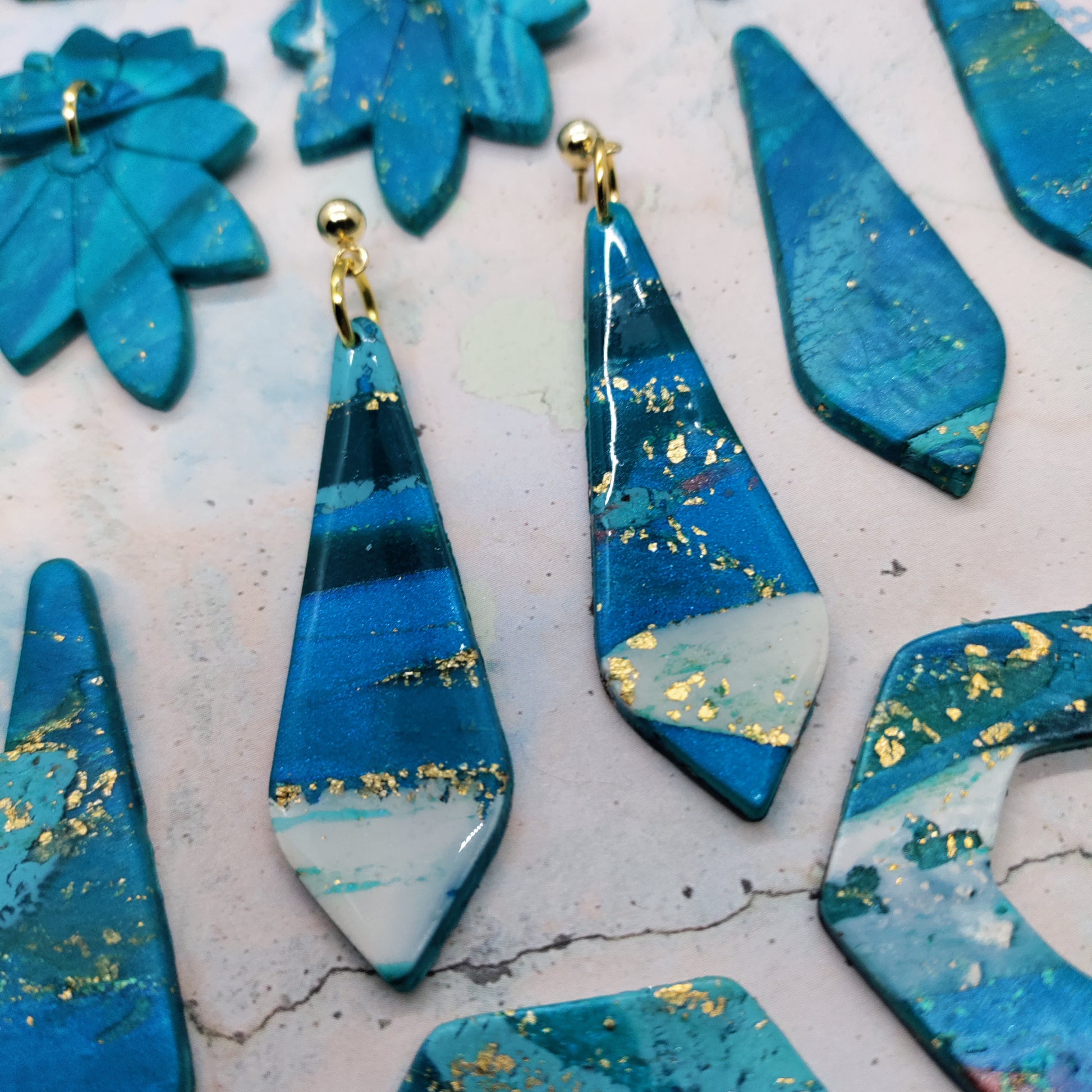 Blue teardrop earrings with gold flakes on a textured surface
