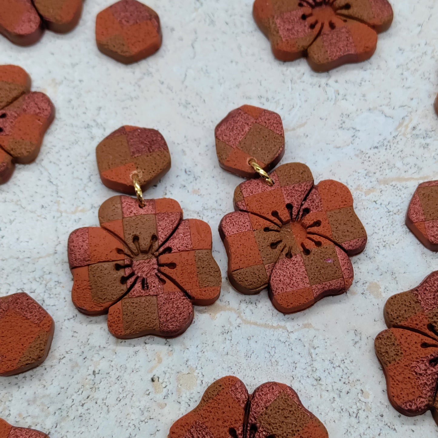 Pair of floral-shaped earrings with a checkered pattern on a textured surface.