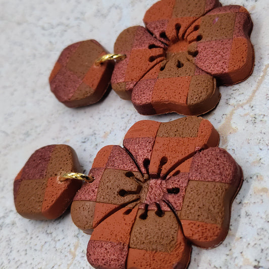 Pair of flower-shaped earrings with a patchwork design on a textured surface.
