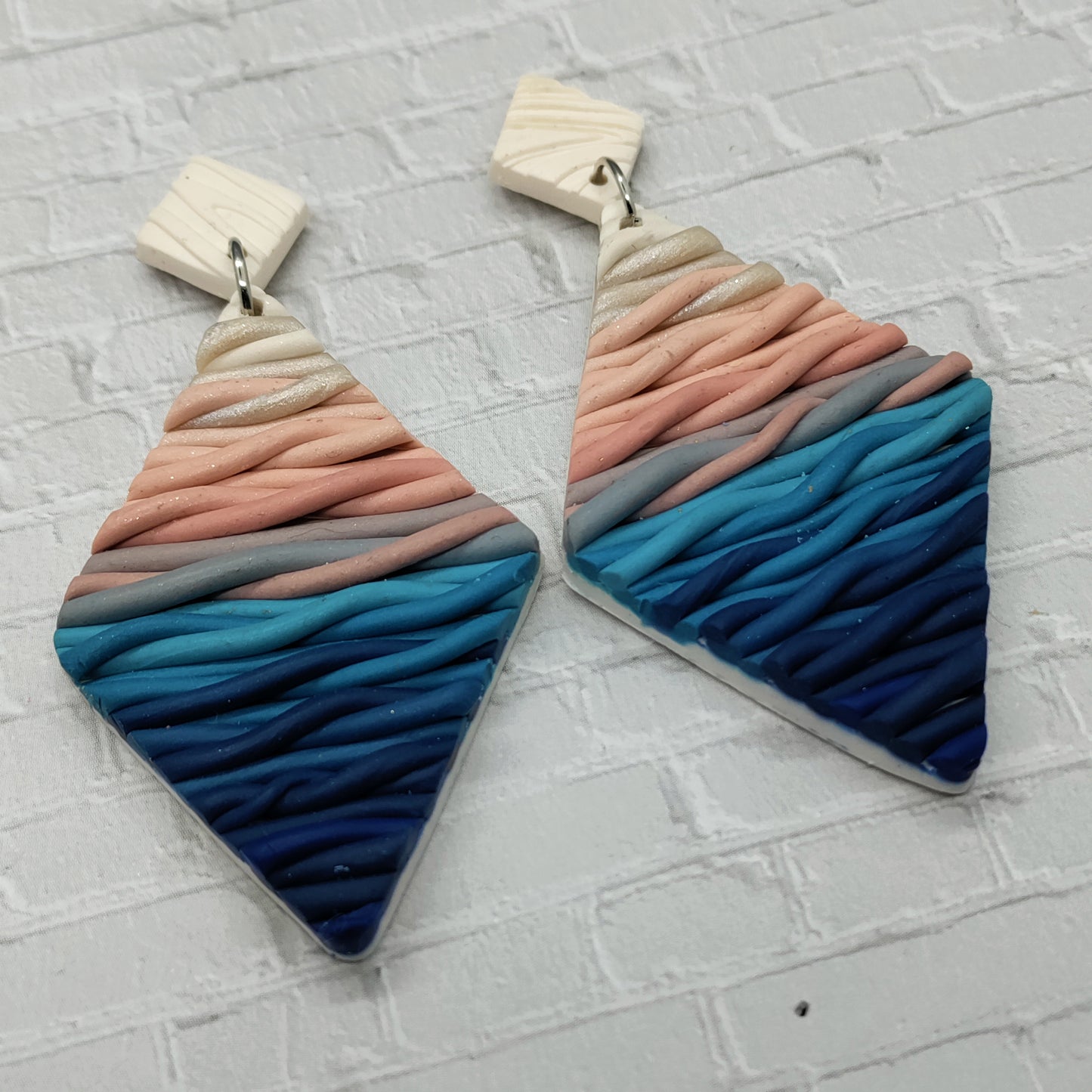 Pair of colorful earrings with wavy pattern on a textured gray surface