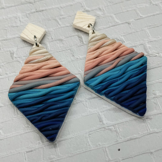 Pair of colorful earrings with wavy pattern on a textured gray surface