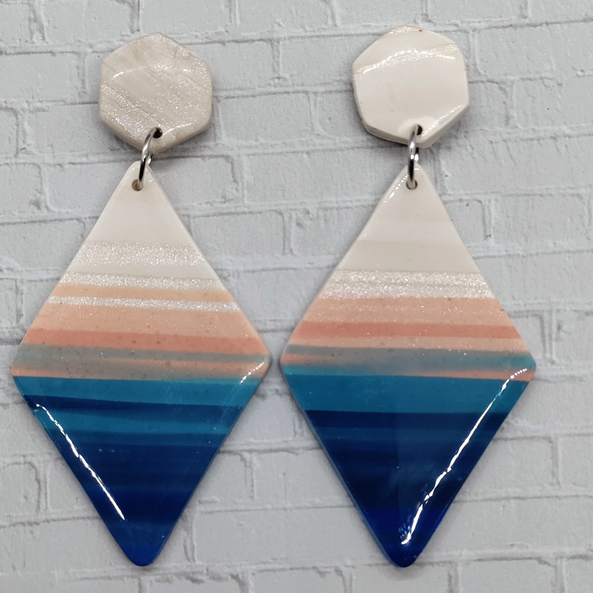 Geometric earrings with blue, pink, and white stripes on a light gray background