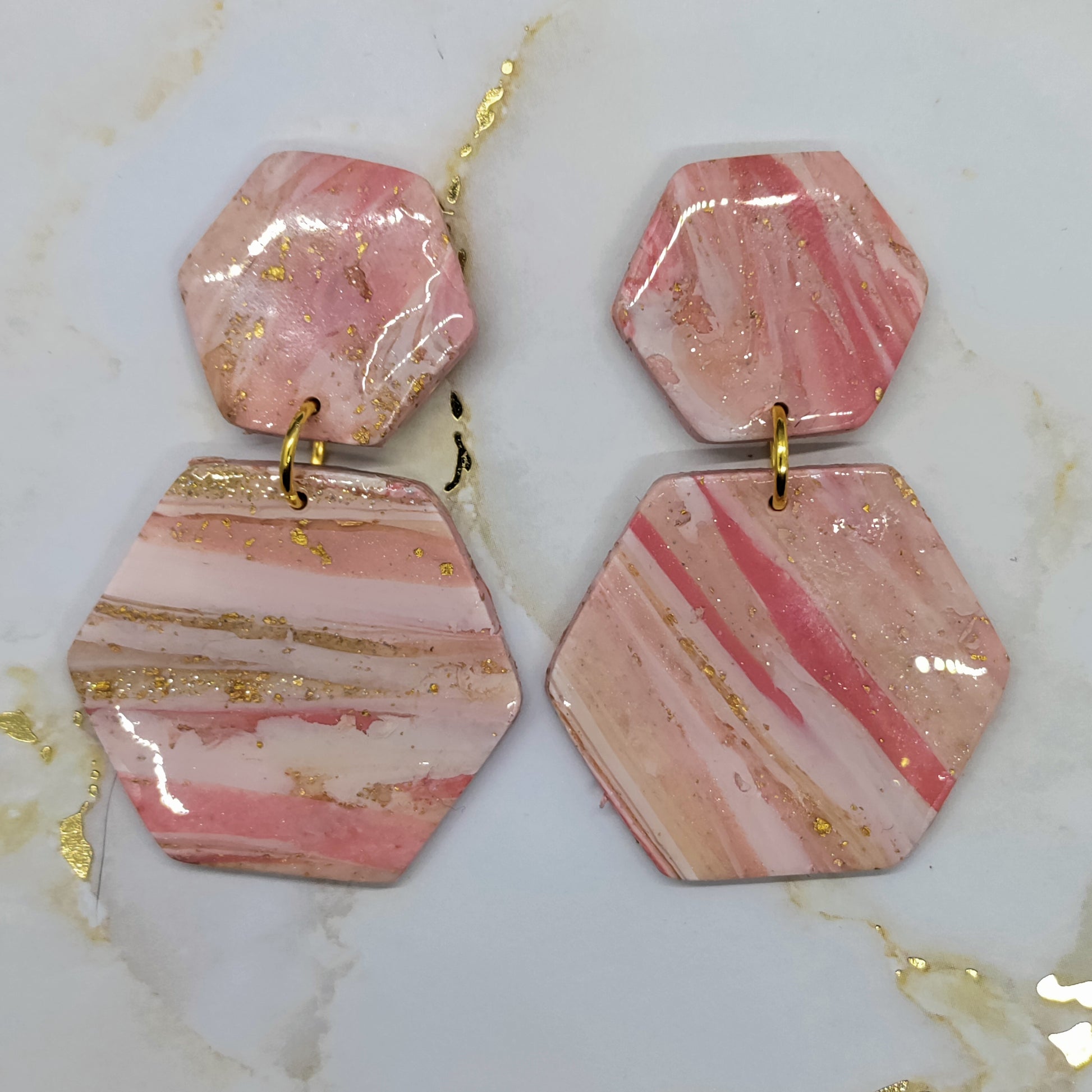 Hexagonal pink and gold earrings on a marble surface