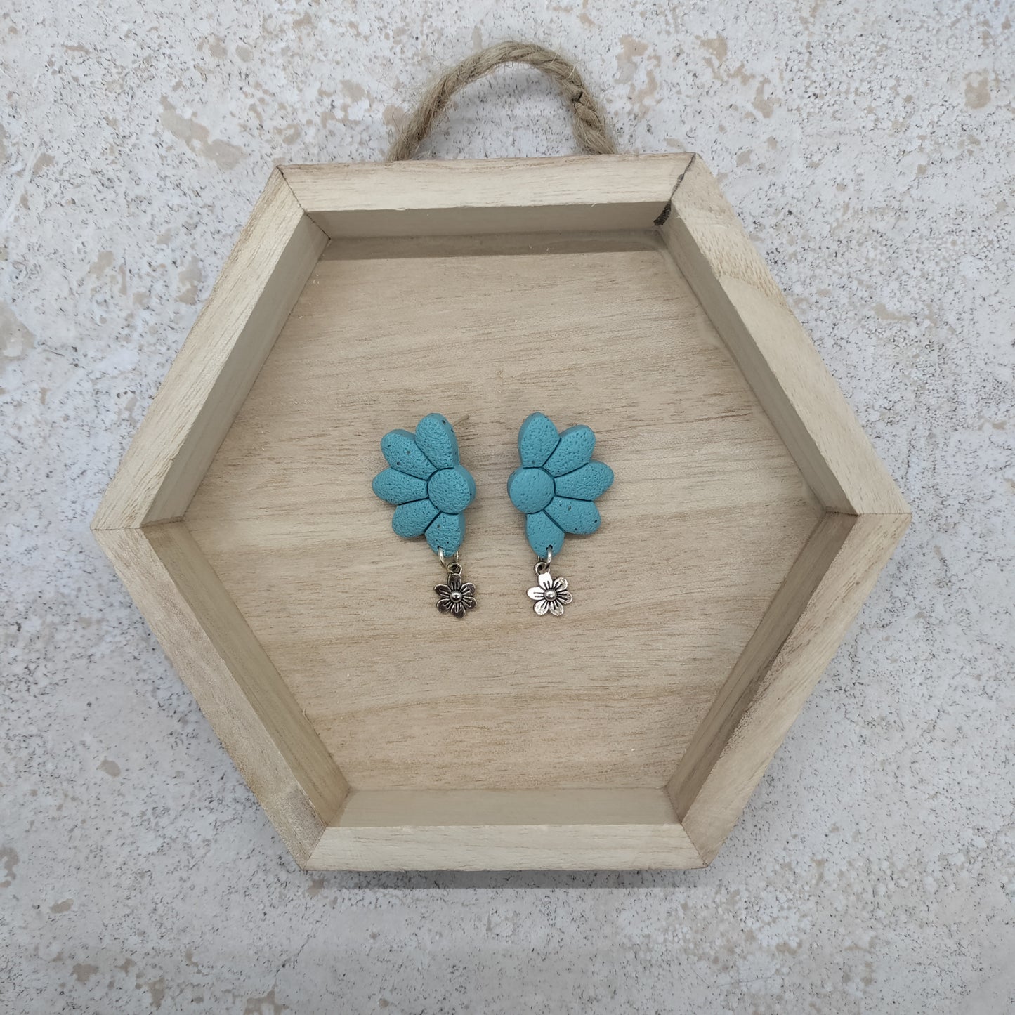 Hexagonal wooden tray with blue floral earrings on a textured surface