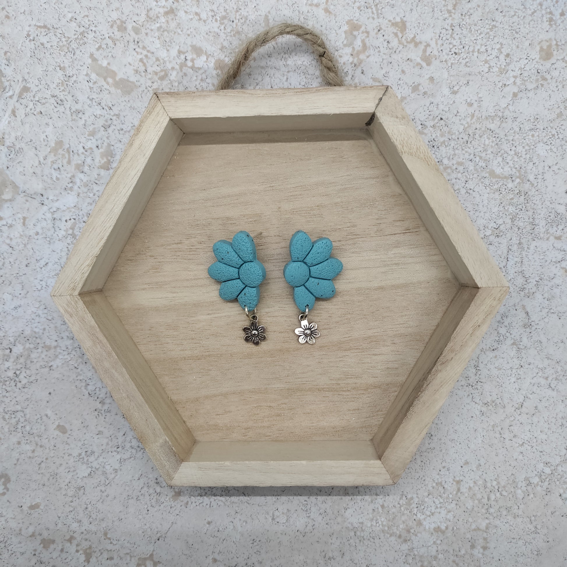 Hexagonal wooden tray with blue floral earrings on a textured surface