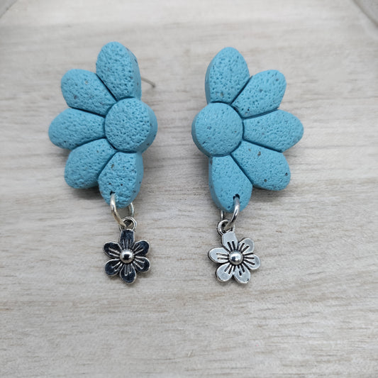 Pair of blue flower-shaped earrings with silver charms on a light wooden surface.
