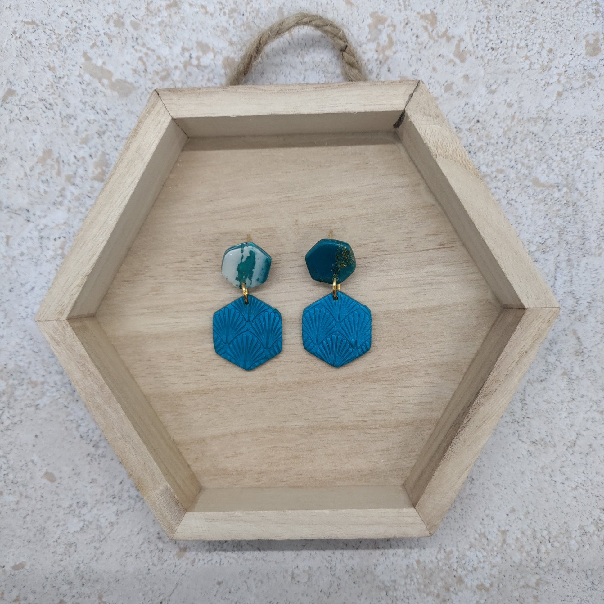 Hexagonal wooden tray with blue earrings on a textured surface