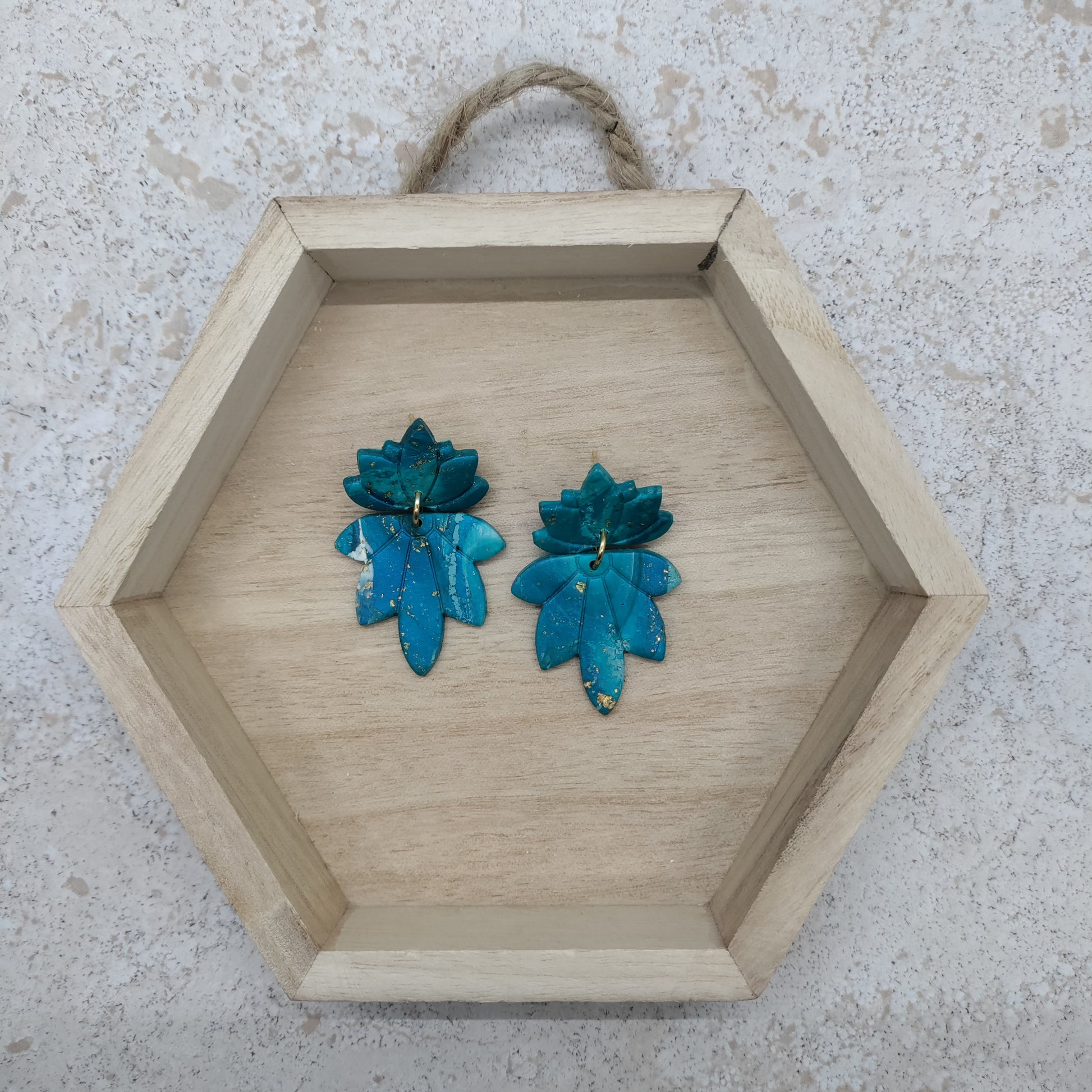 Hexagonal wooden tray with teal floral earrings on a textured surface