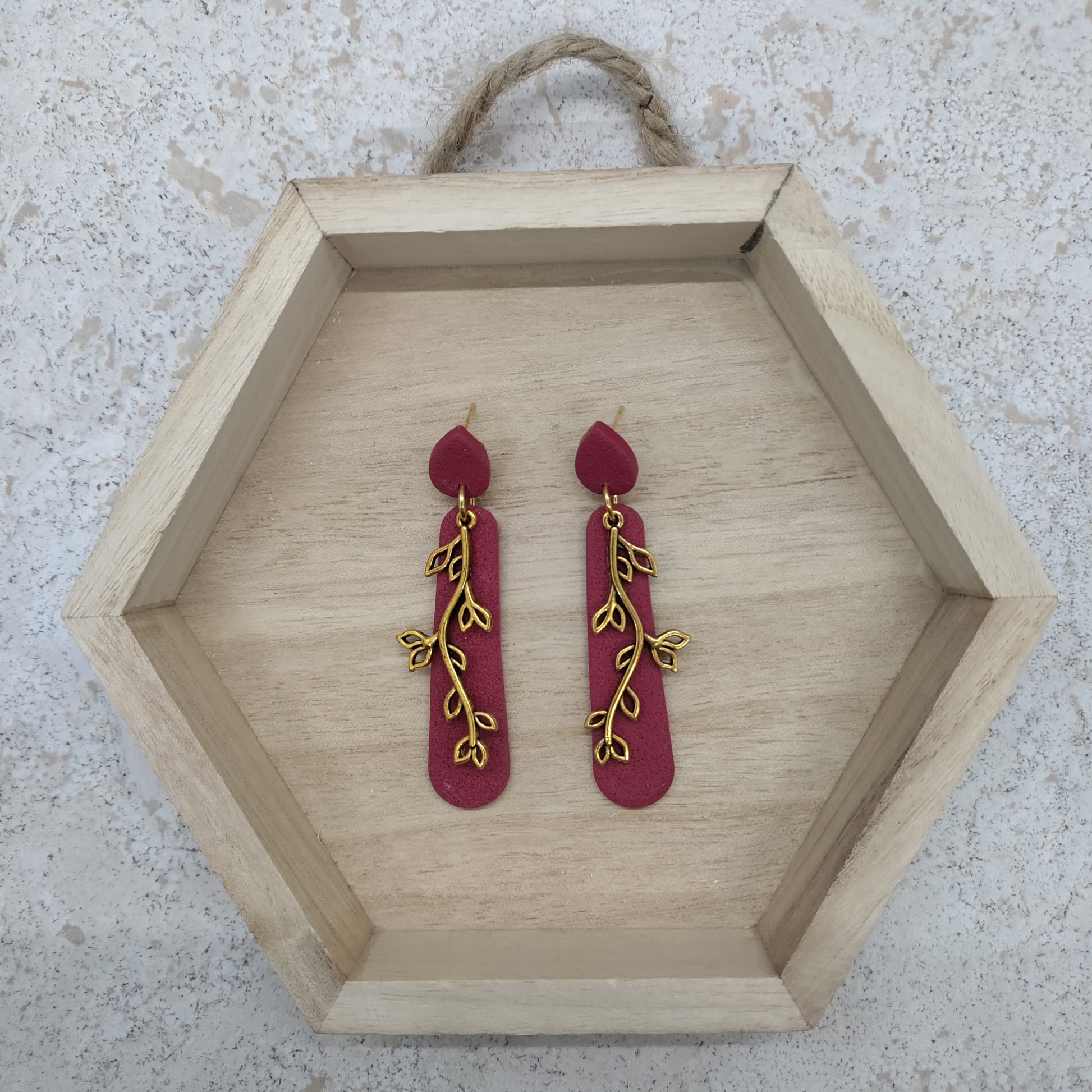 Red earrings with gold leaf designs on a wooden hexagonal tray.