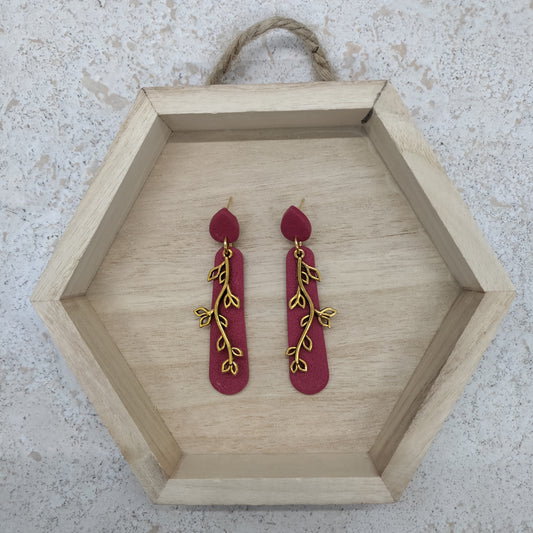 Red earrings with gold leaf designs on a wooden hexagonal tray.