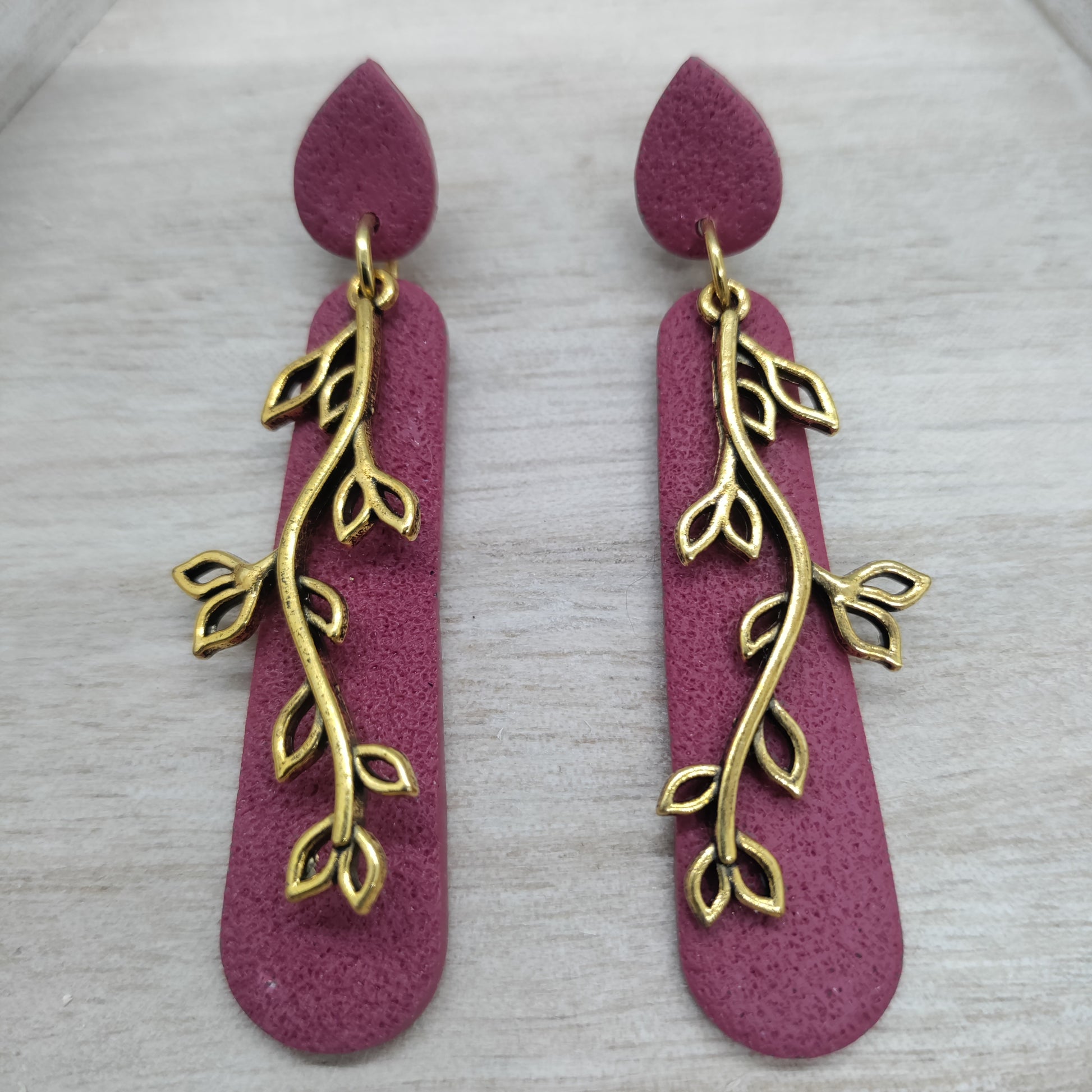 Pair of earrings with gold leaf design on a pink background
