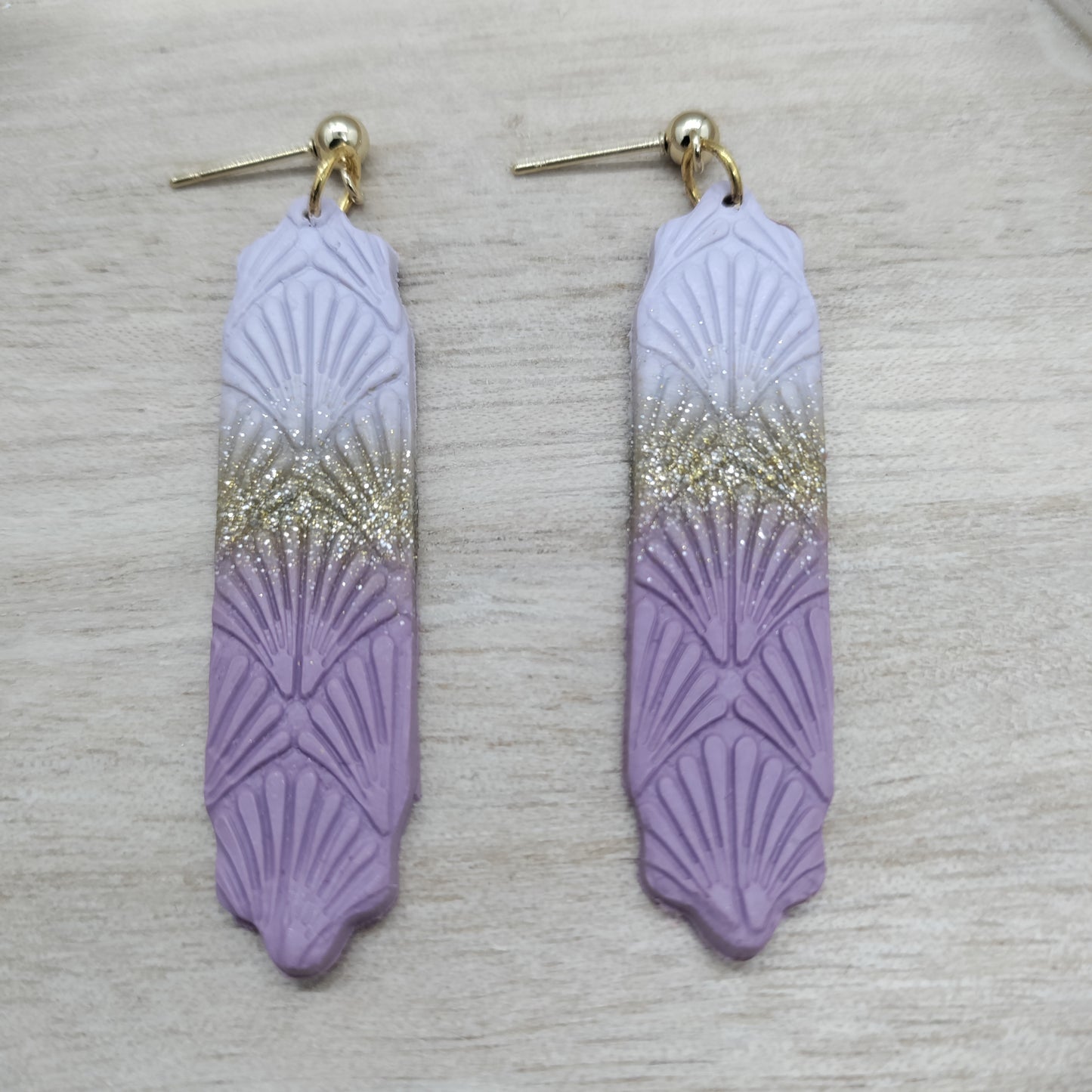 Pair of purple feather-shaped earrings with gold gradient on a light gray background