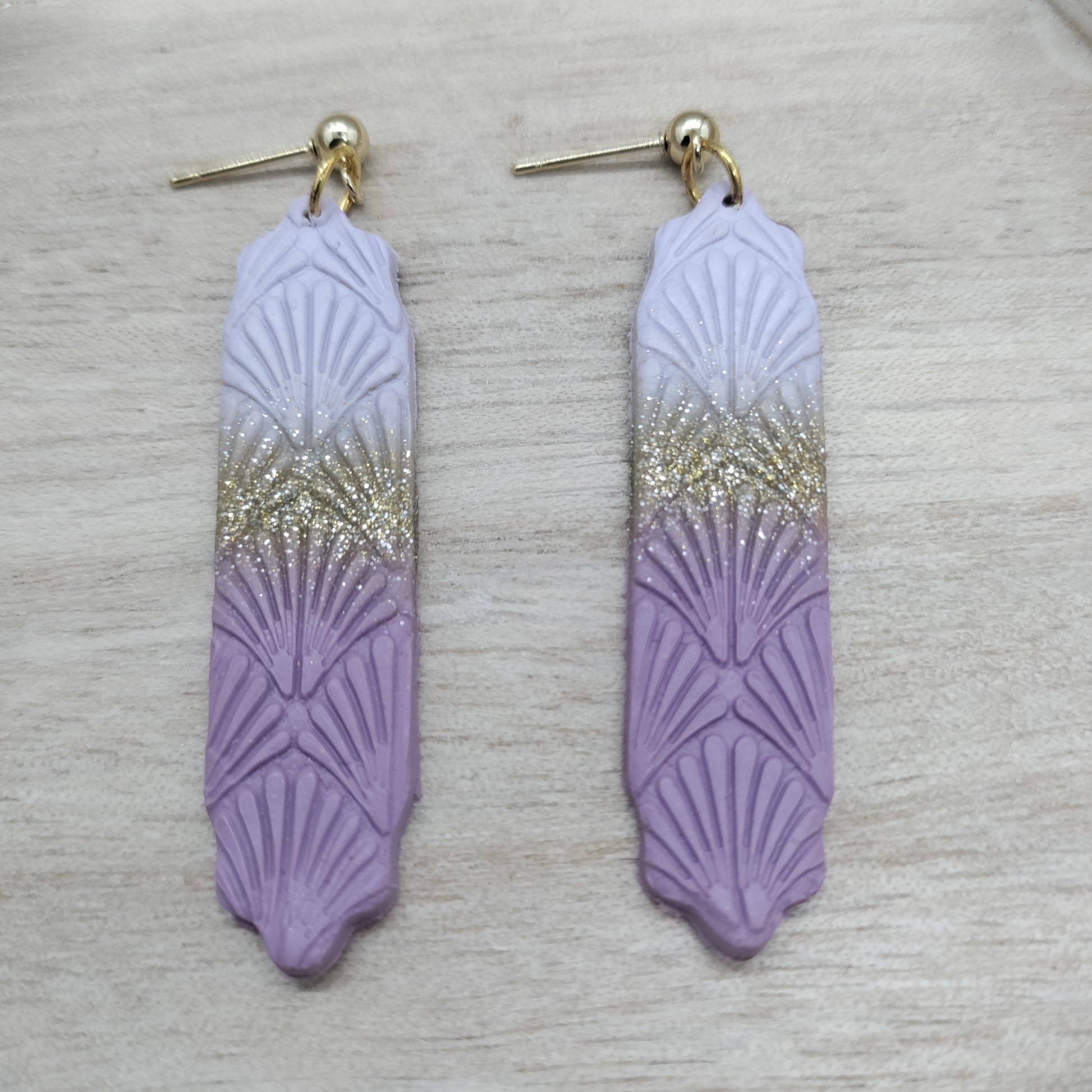 Pair of purple feather-shaped earrings with gold gradient on a light gray background