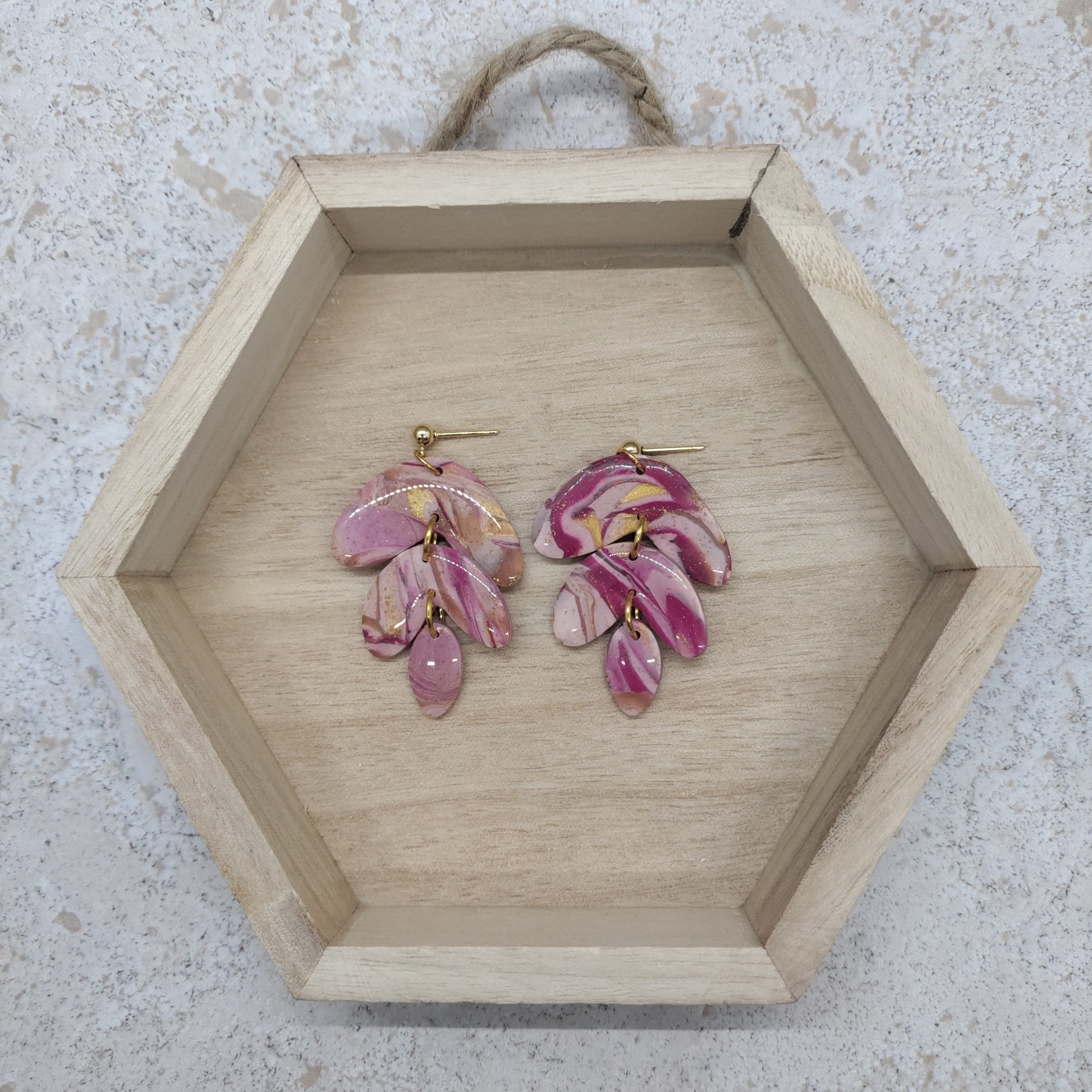 Pink floral earrings on a wooden hexagonal tray with a textured background