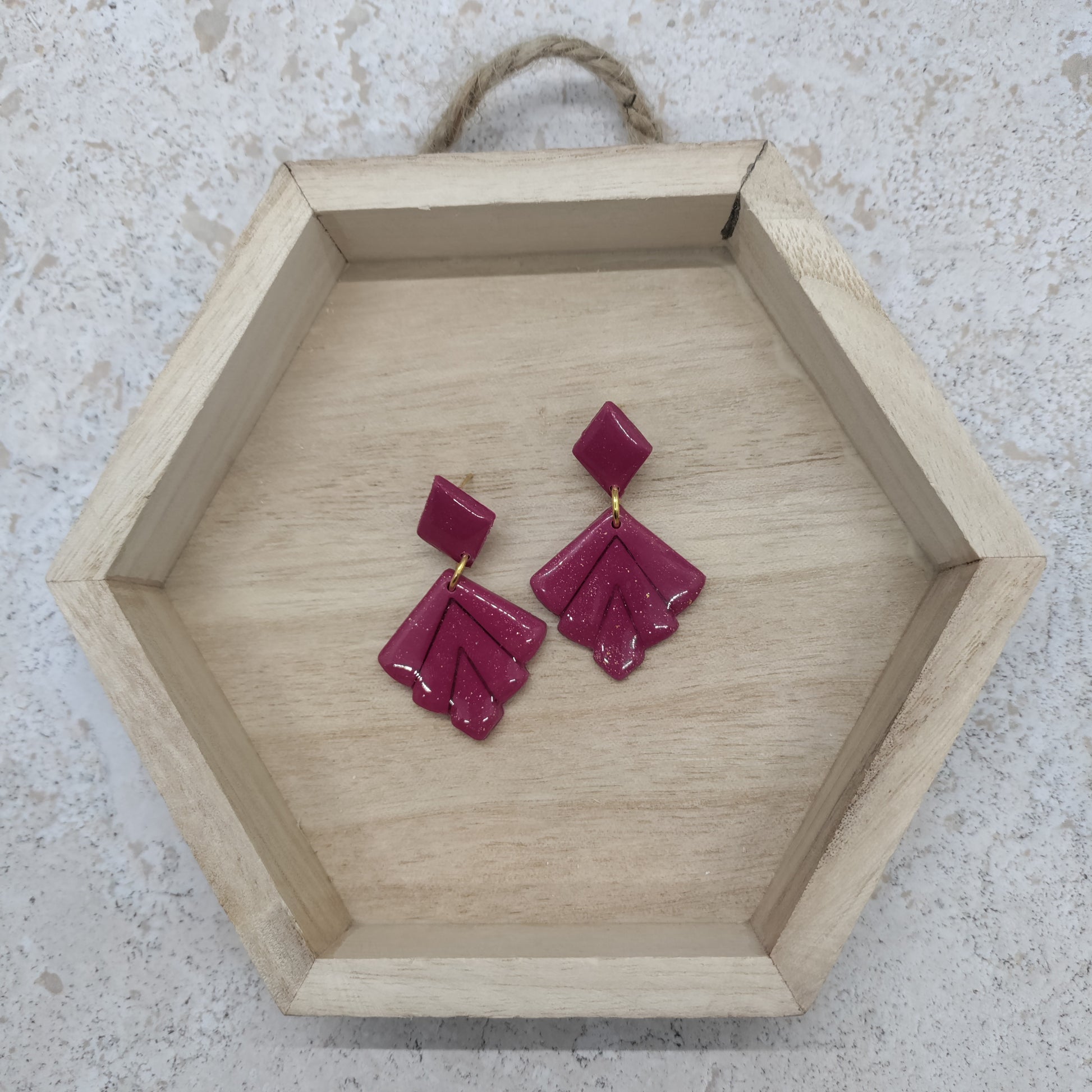 Hexagonal wooden tray with pink earrings on a light stone background
