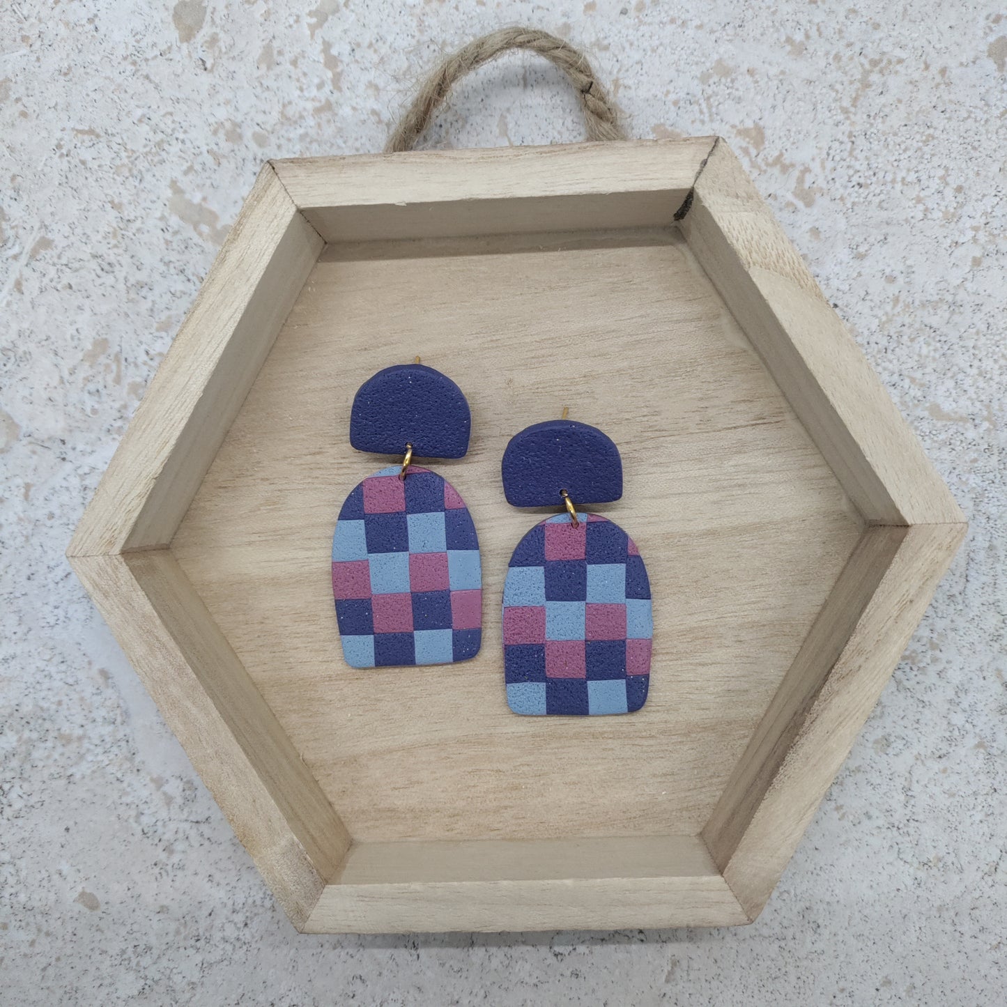 Checkered earrings on a wooden hexagonal tray against a textured surface