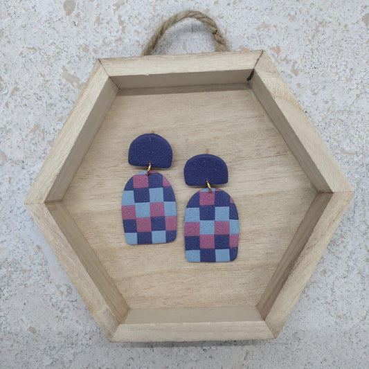 Checkered earrings on a wooden hexagonal tray against a textured surface