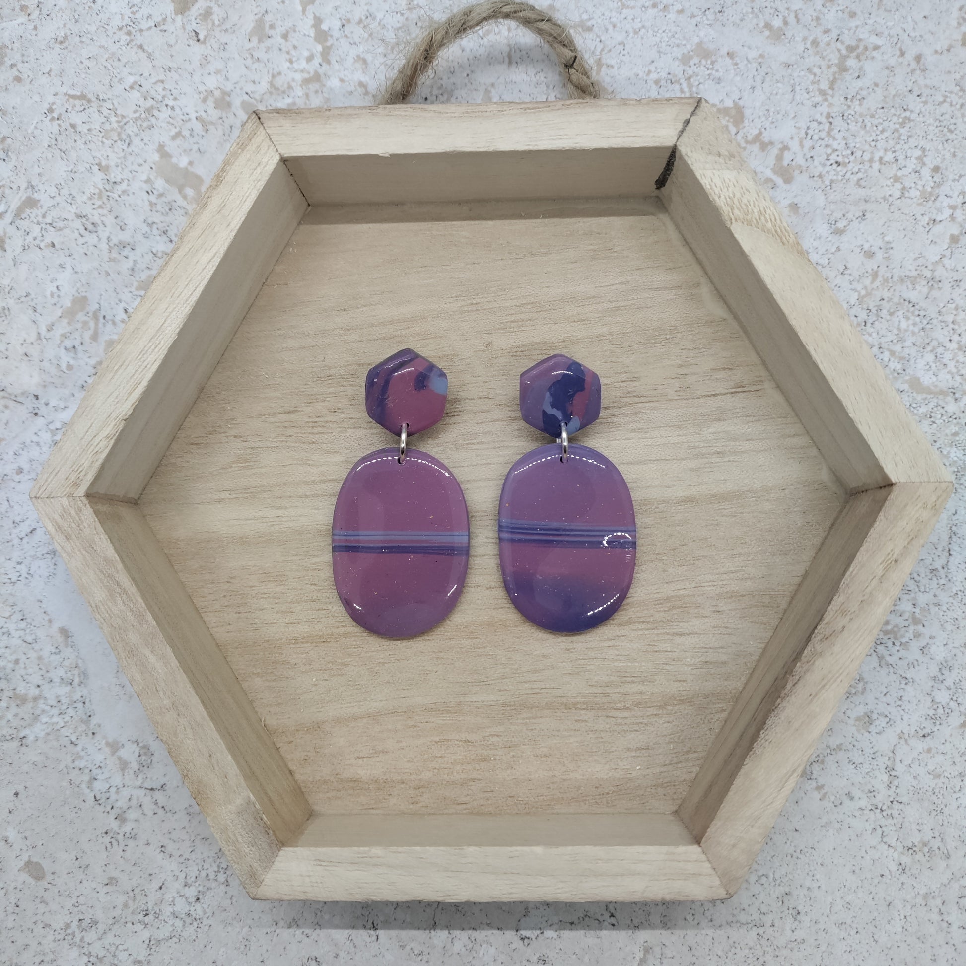 Hexagonal wooden tray with purple earrings on a textured surface