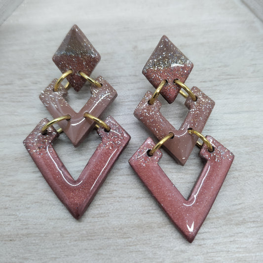Pair of geometric earrings with pink and gold design on a light gray background