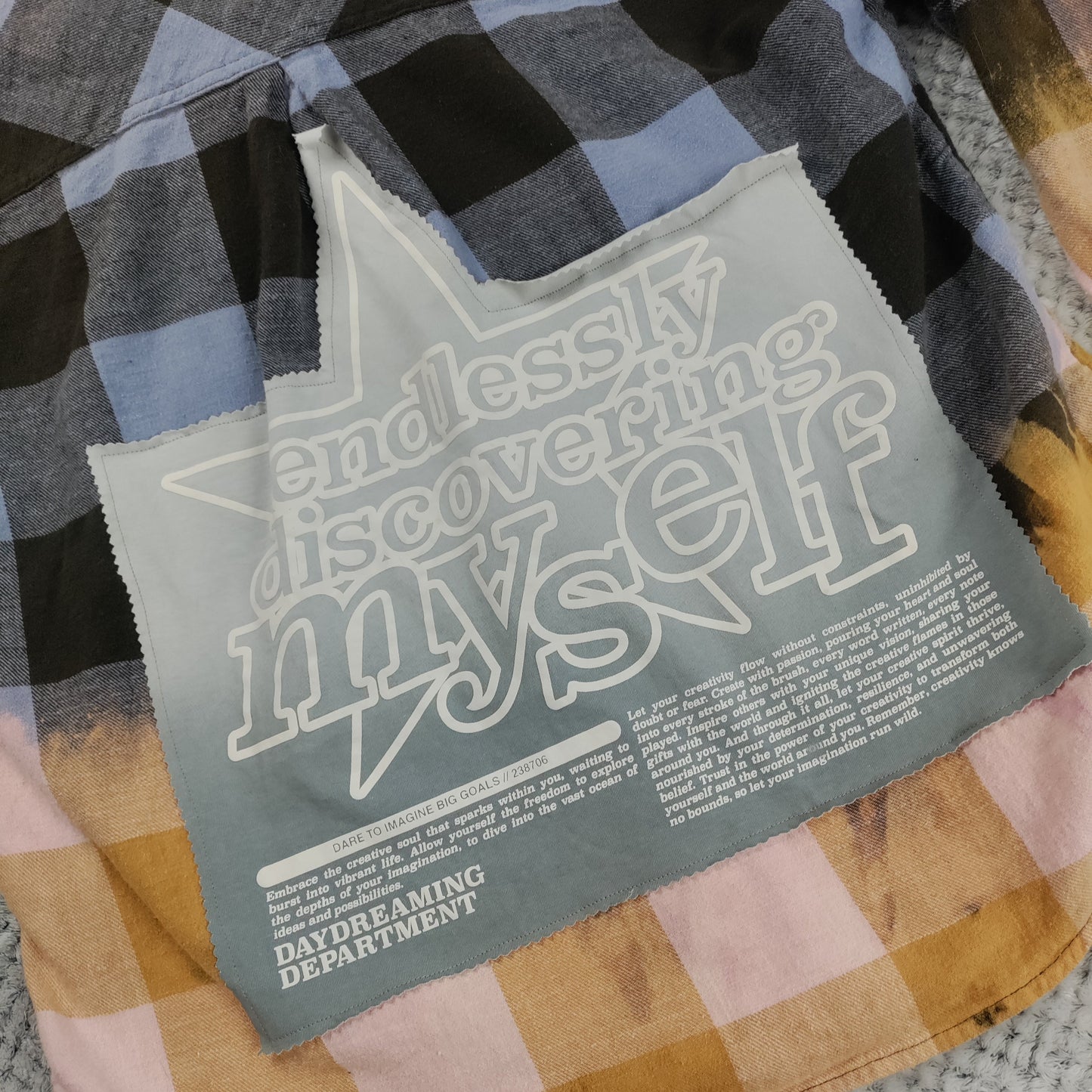 Plaid shirt with a label reading 'Endlessly discovering myself' on a textured surface.