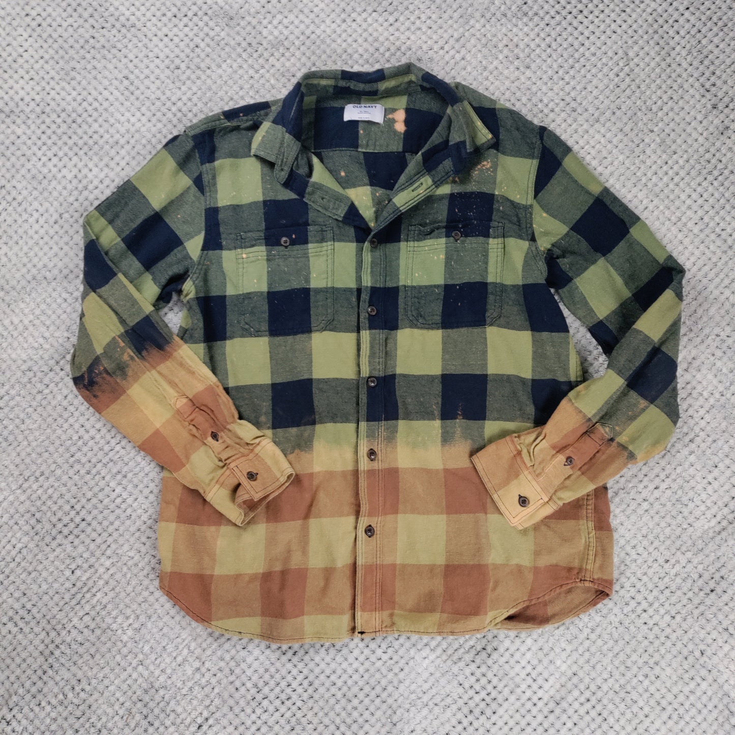 Plaid shirt with green, blue, and brown colors on a textured gray background