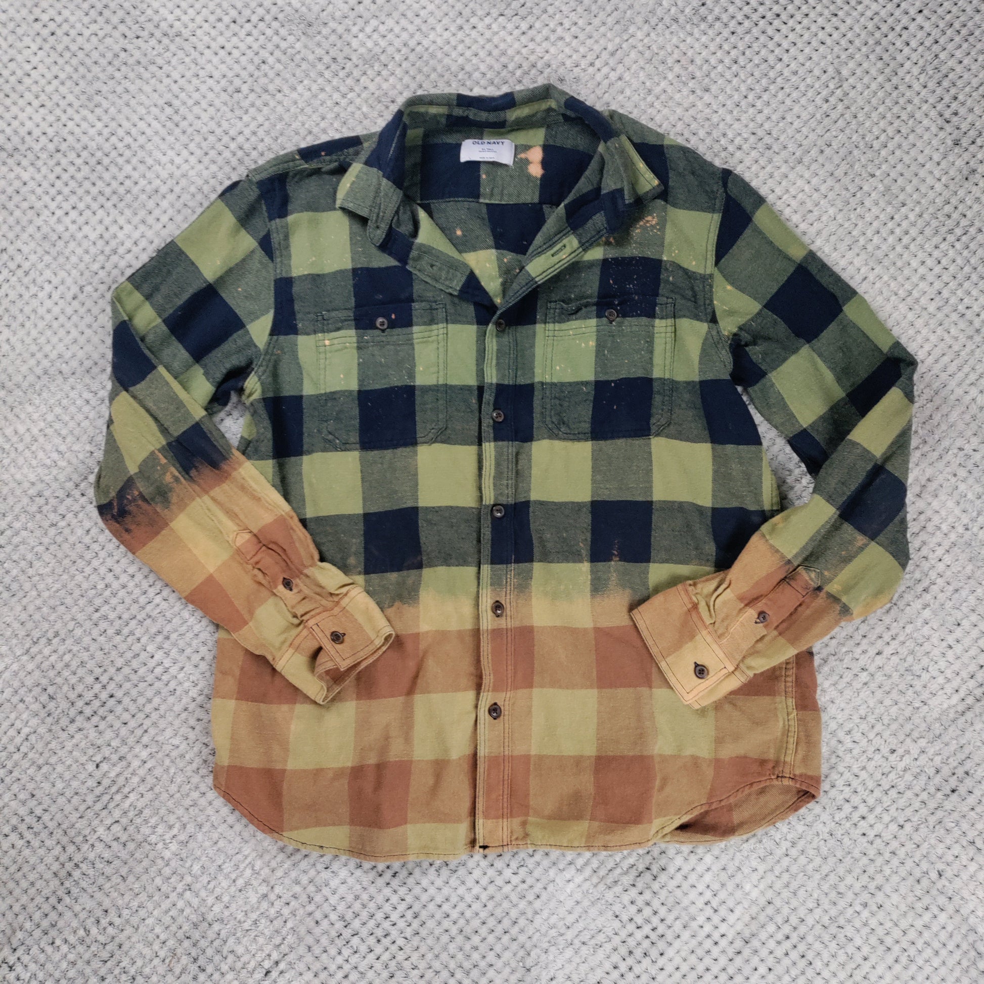 Plaid shirt with green, blue, and brown colors on a textured gray background