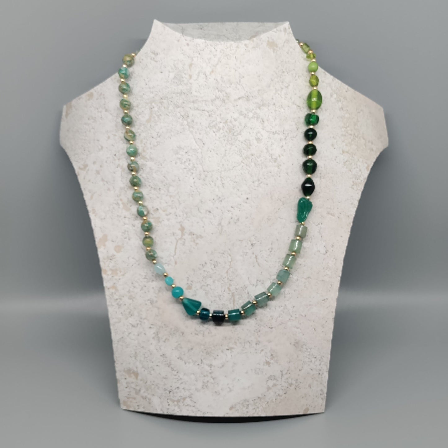 Necklace with green and black beads on a mannequin bust against a gray background