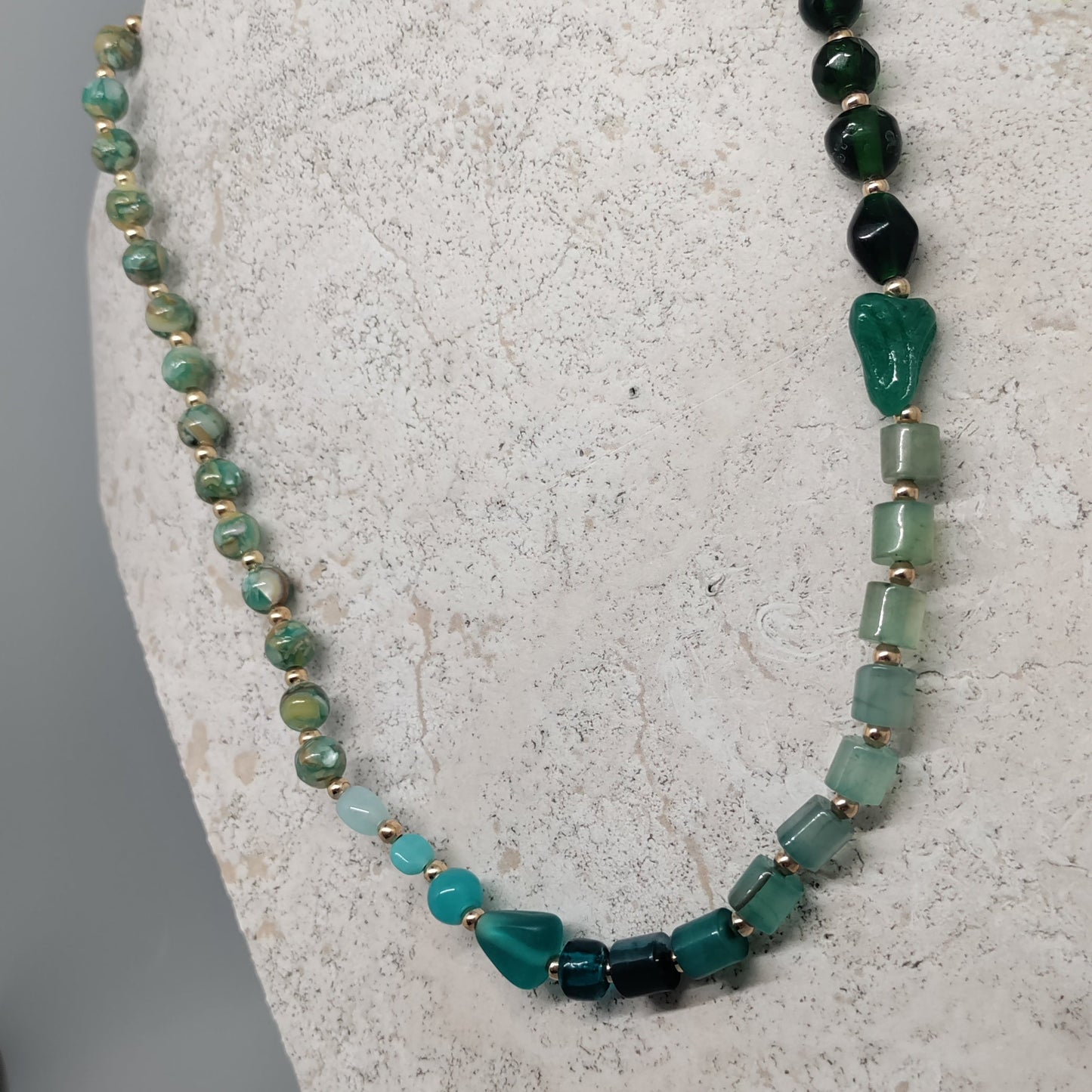 Necklace with green and black beads on a white stand against a gray background