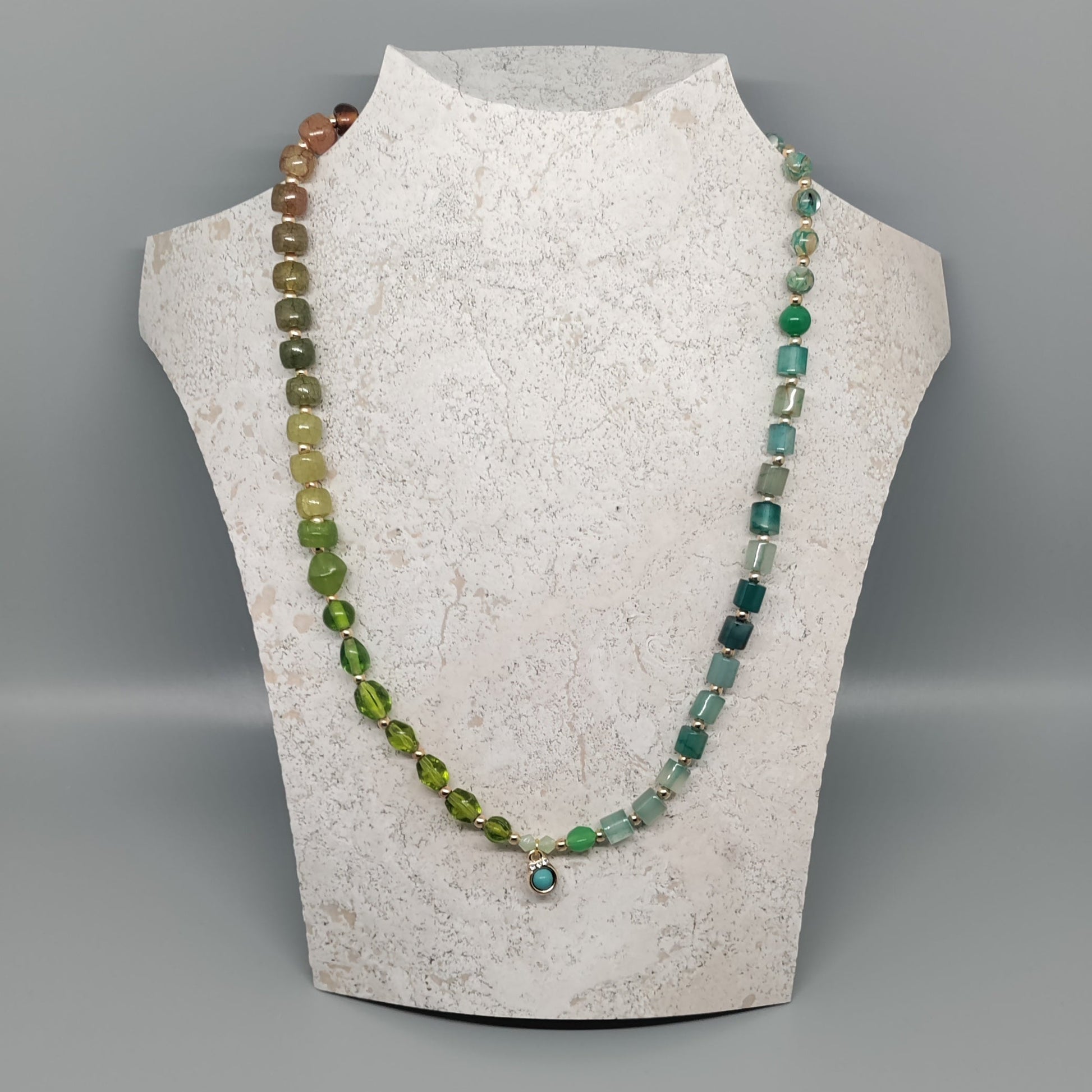 Necklace with green beads on a mannequin bust against a gray background