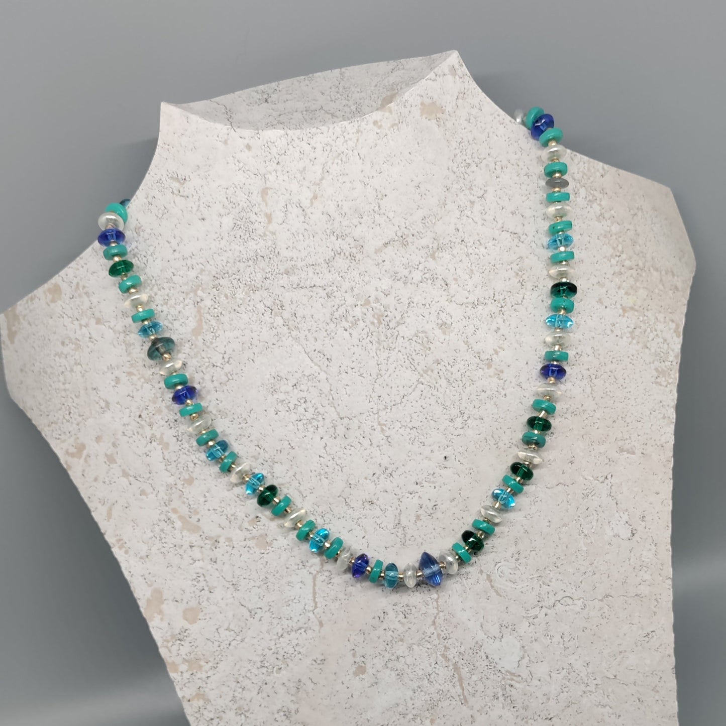 Necklace with blue and green beads on a mannequin bust against a gray background