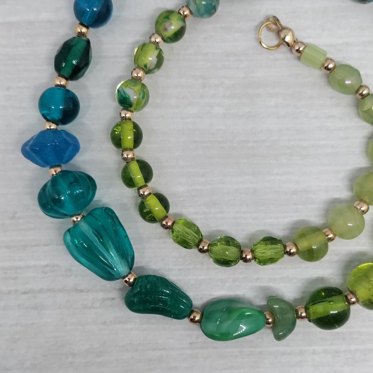 Beaded necklace with green and blue beads on a textured surface