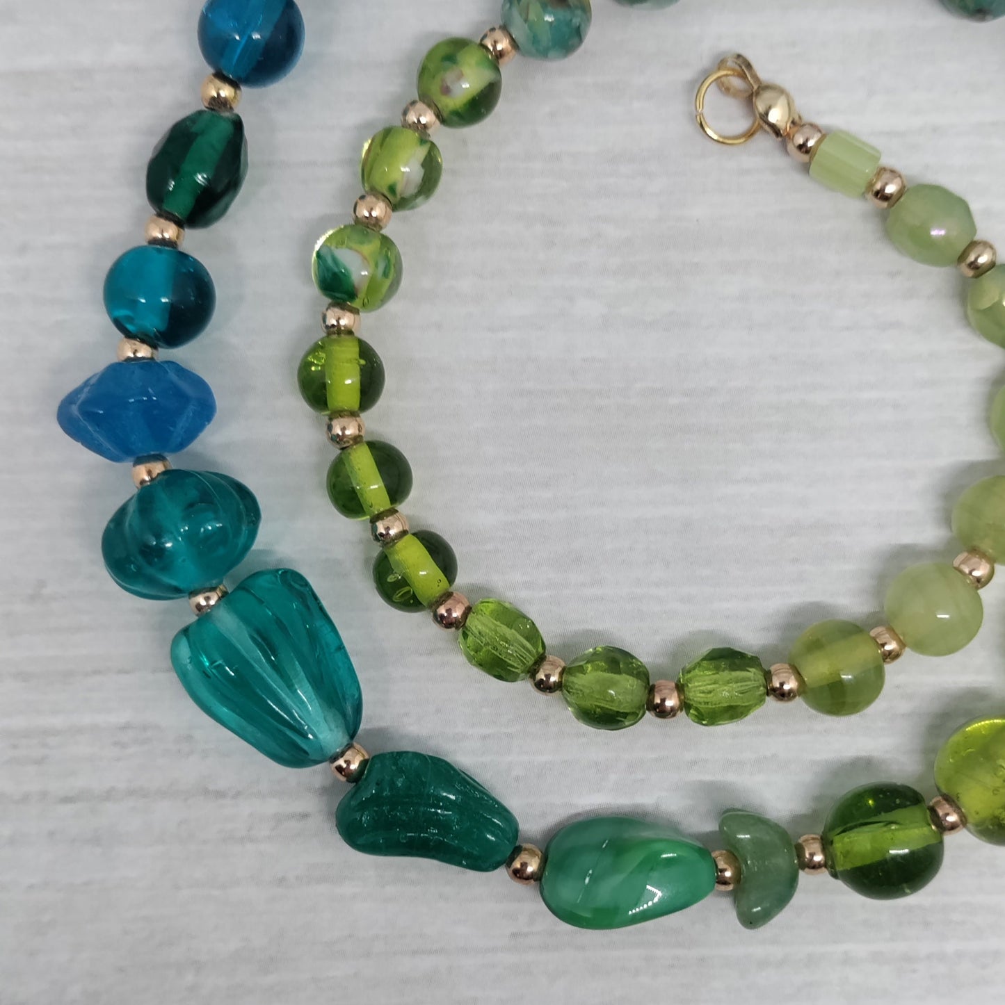 Beaded necklace with green and blue beads on a textured surface