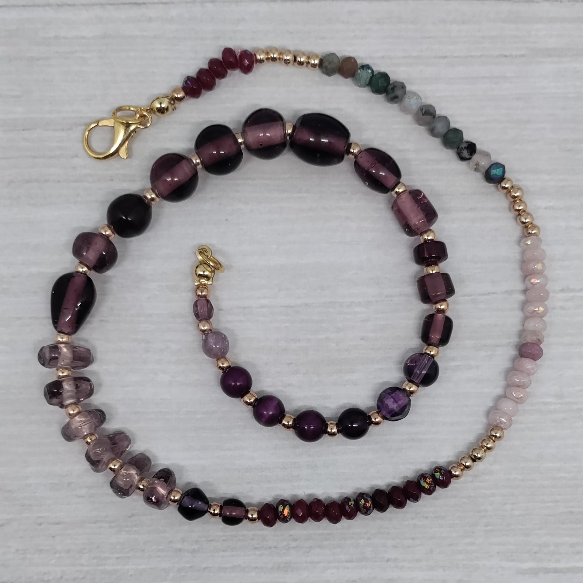 Beaded necklace with purple and gold accents on a light gray background