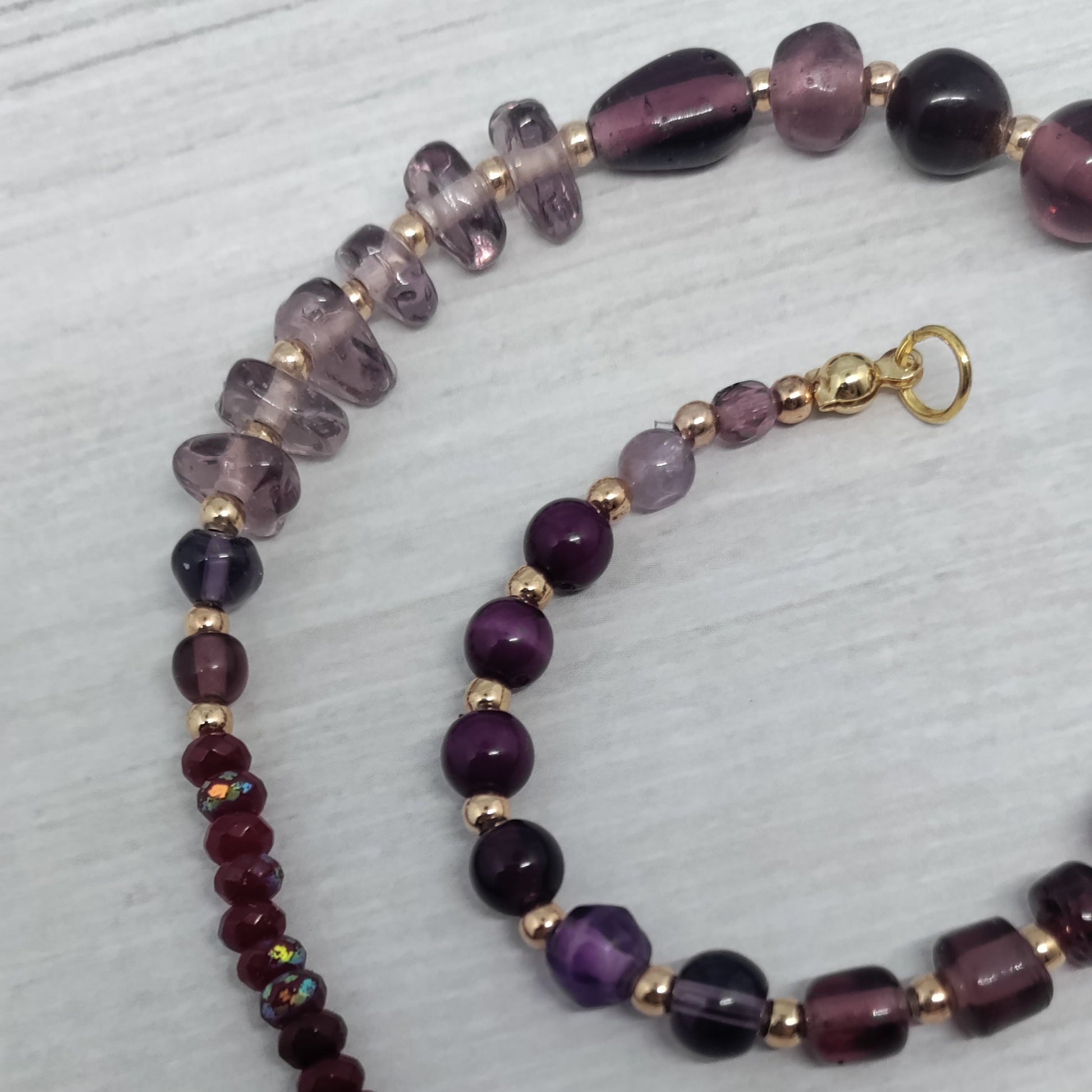 Beaded necklace with purple and gold accents on a light gray background