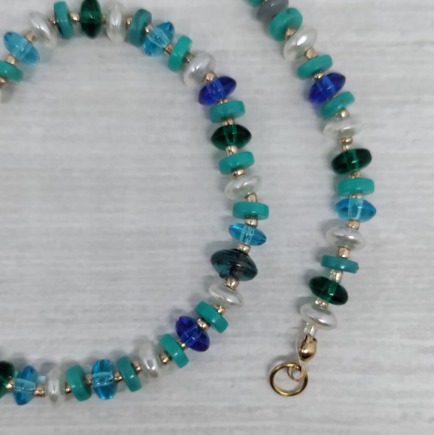 Necklace with blue, green, and silver beads on a light gray background
