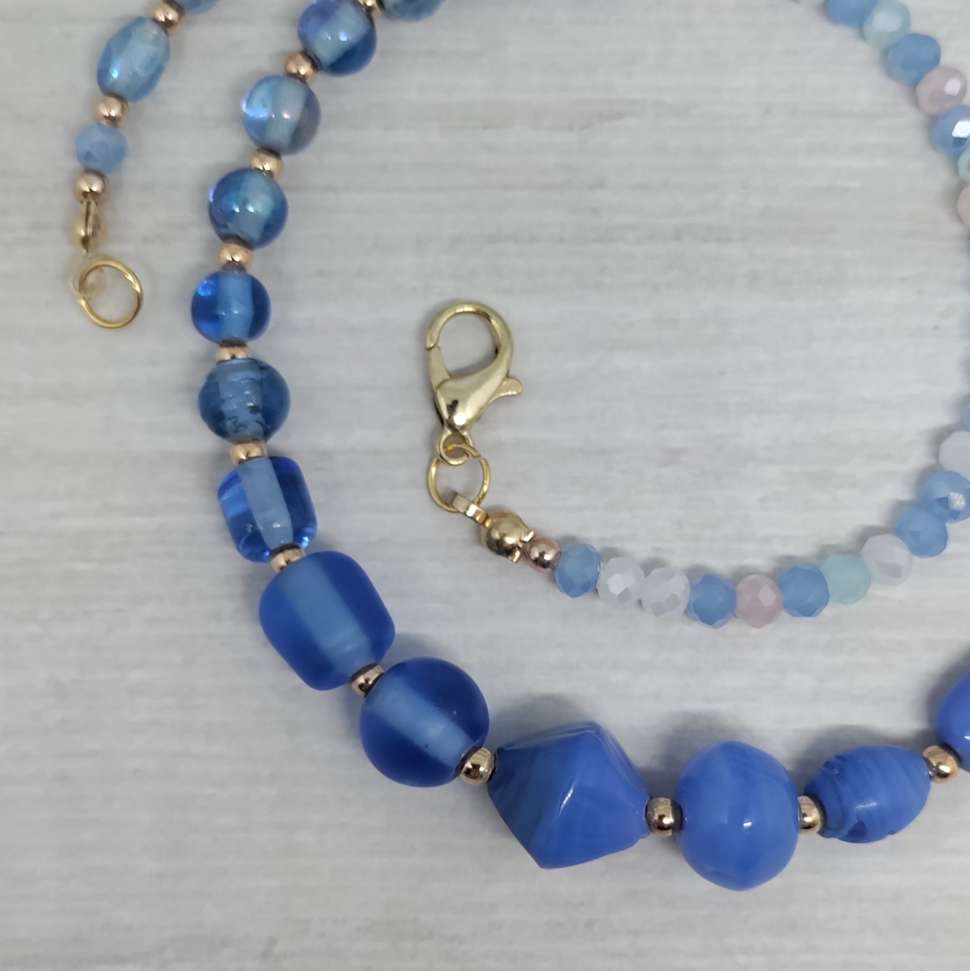 Blue beaded necklace with gold accents on a light gray background