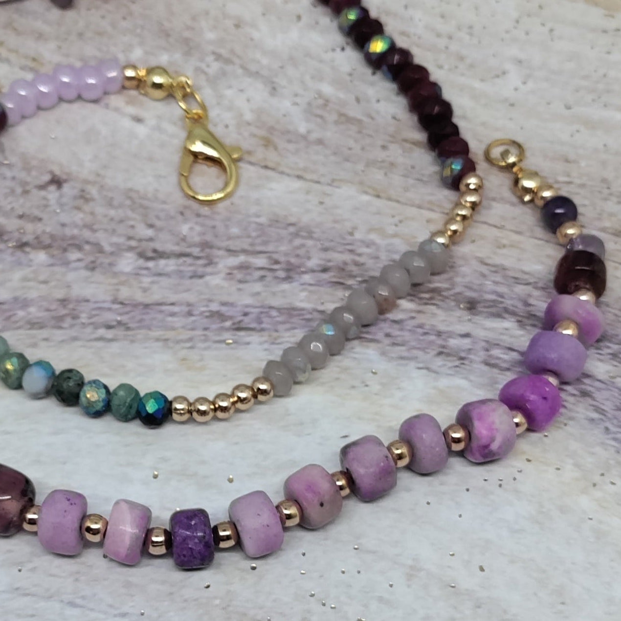 Purple and green gemstone beaded necklace on a textured surface