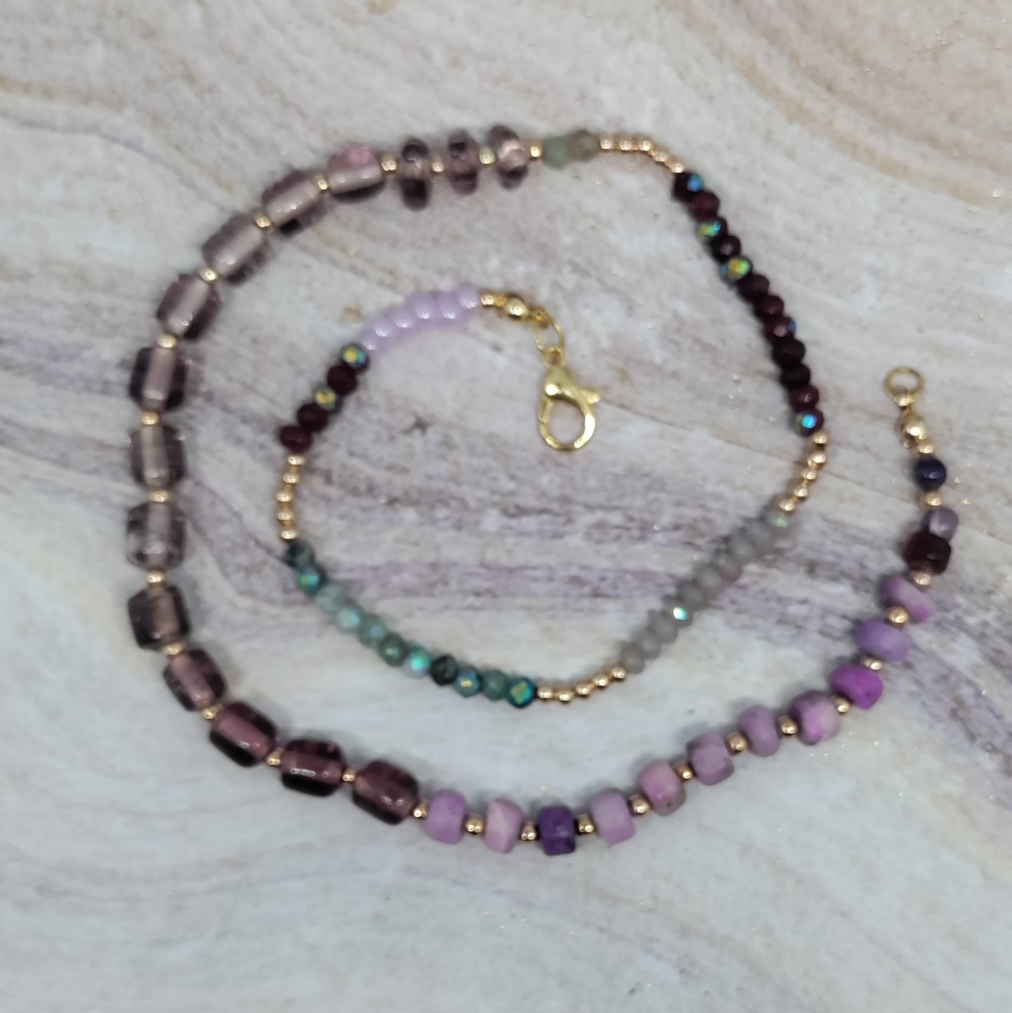 Purple and green gemstone beaded necklace on a textured surface