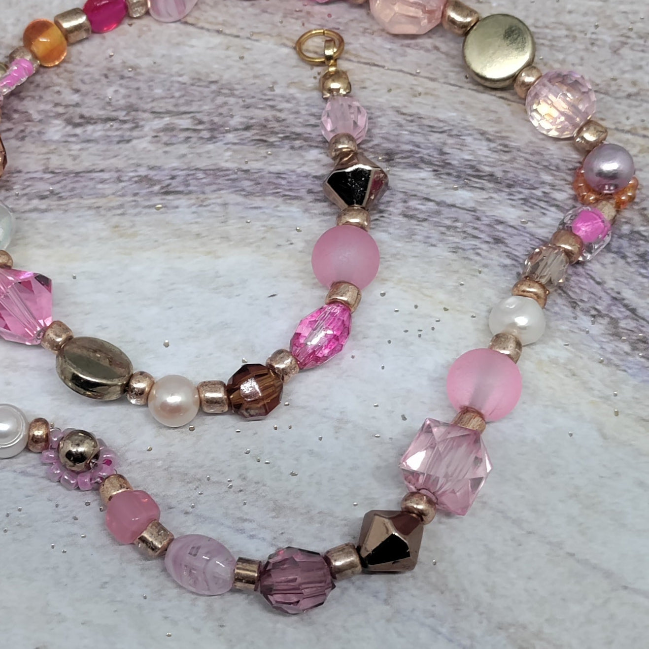 Beaded necklace with pink and gold beads on a marble surface