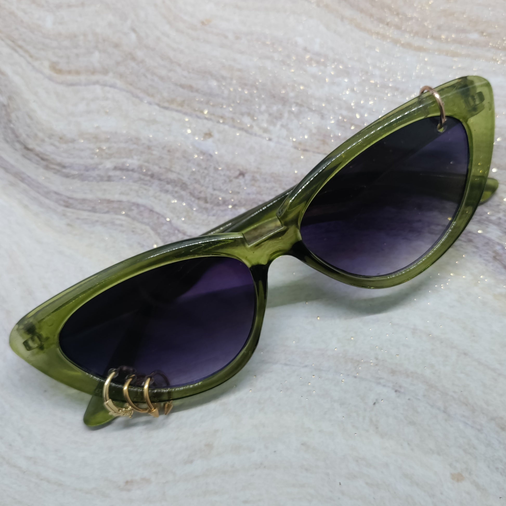 Oversized cat-eye sunglasses with translucent olive green frames and dark purple lenses, resting on a white and gray marbled surface.