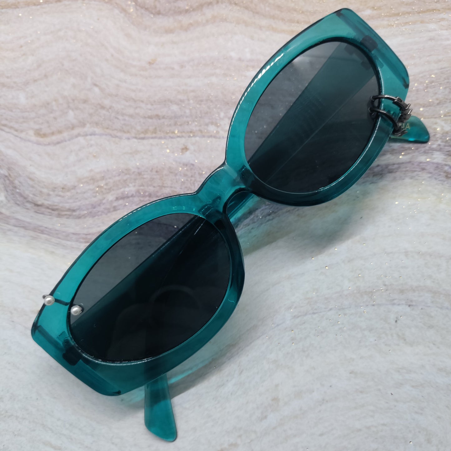 Teal acetate cat-eye sunglasses with dark lenses, resting on a light beige marbled surface.