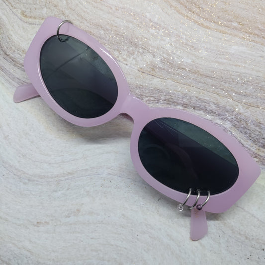 Light purple cat-eye sunglasses with dark lenses and silver hoop earrings, resting on a textured beige marble surface.